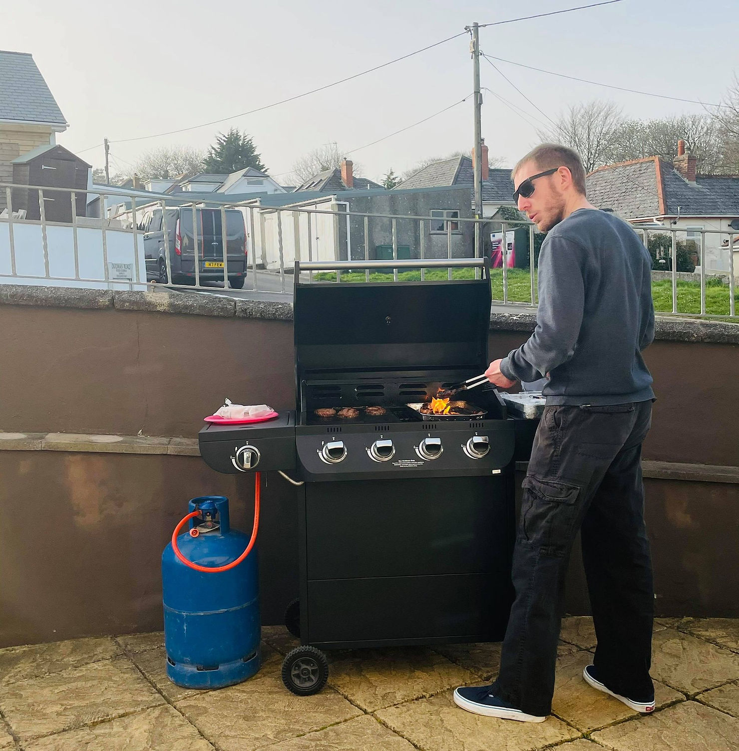 Ross's friend stood at the BBQ with flames coming off the grill