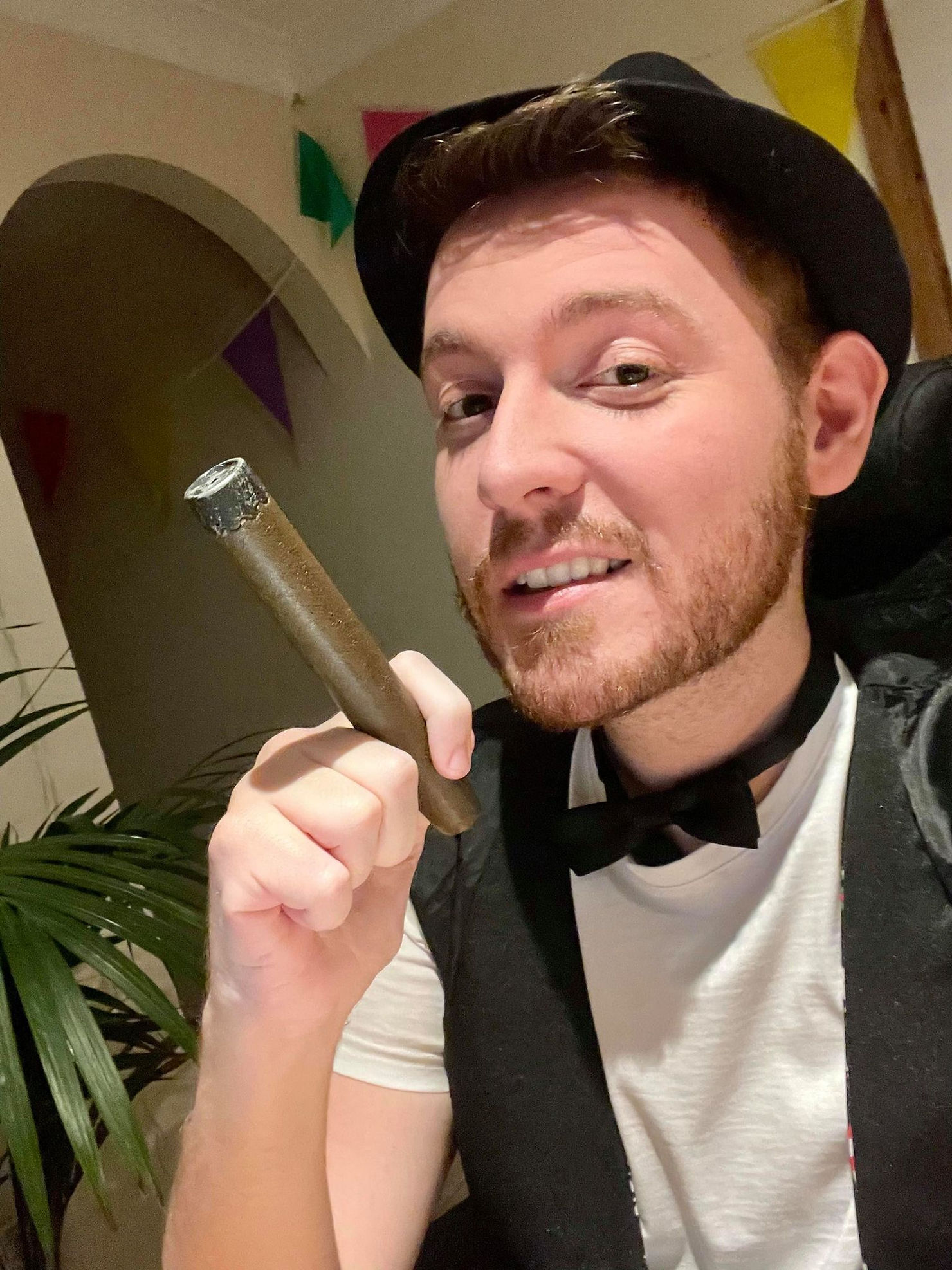 selfie of Ross wearing a white t-shirt and a black waist coat. Top hat, dicky bow tie and a fake cigar in hand.
