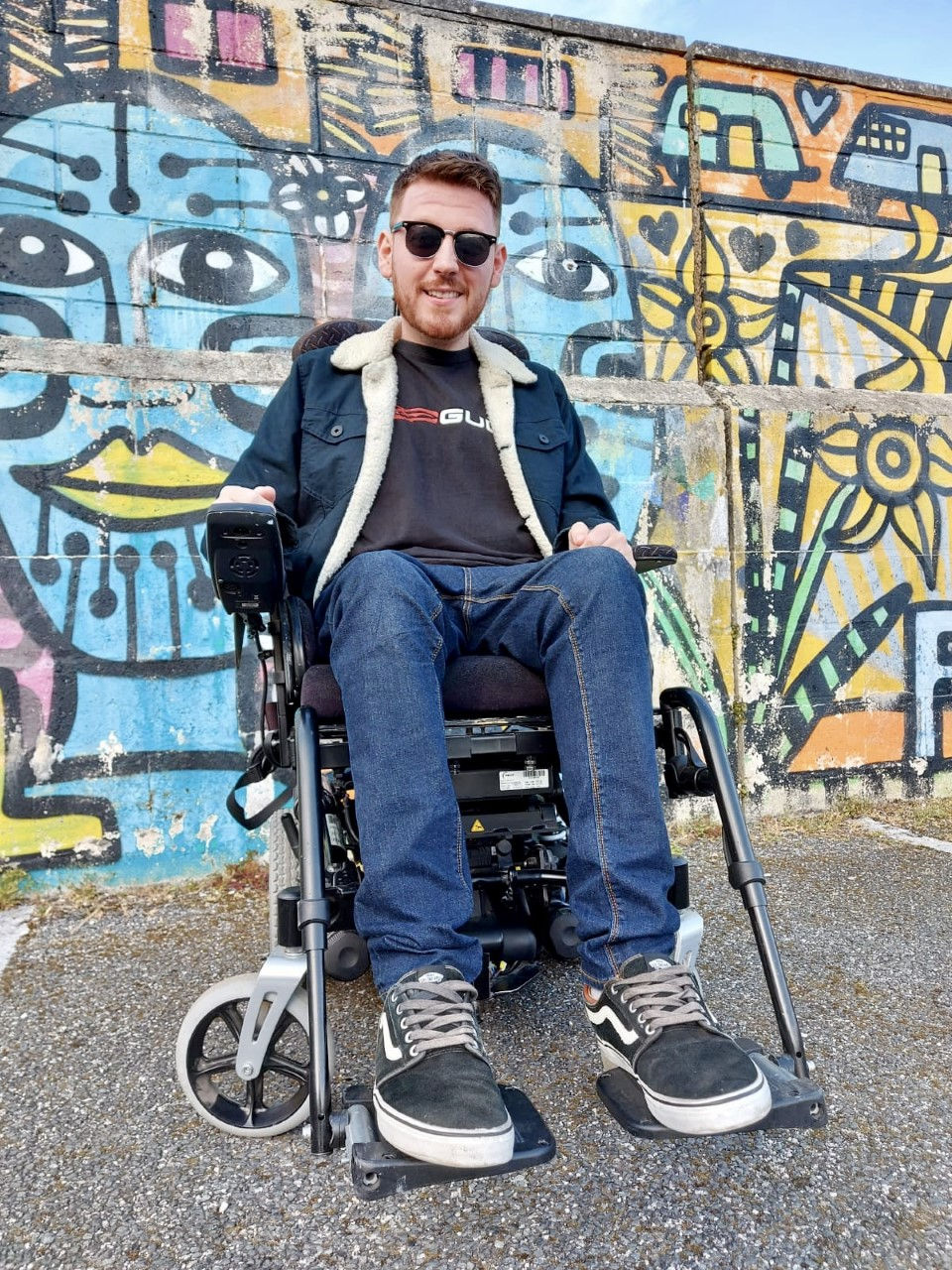 Low down angle of Ross in his wheelchair, sat in front of a multicoloured graffiti wall