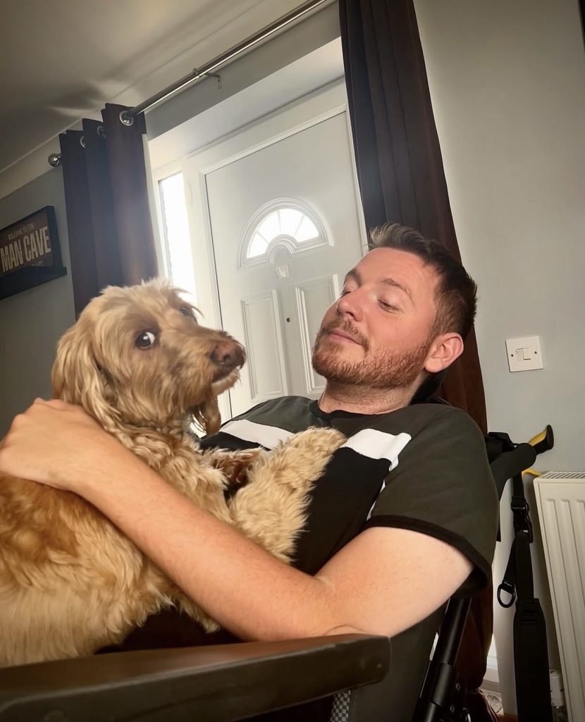 Ross's dog Ralph (cockapoo) laying on his chest, as Ross is reclined back in his wheelchair.